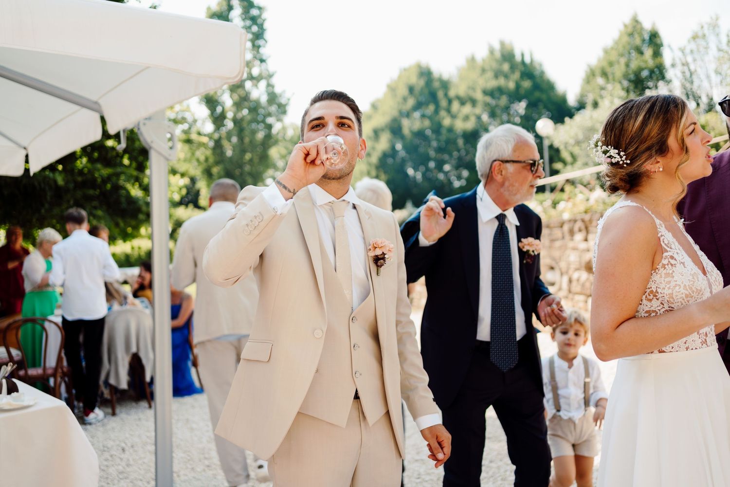 Emotional groom wipes tear at outdoor wedding reception while older guests stand nearby.
