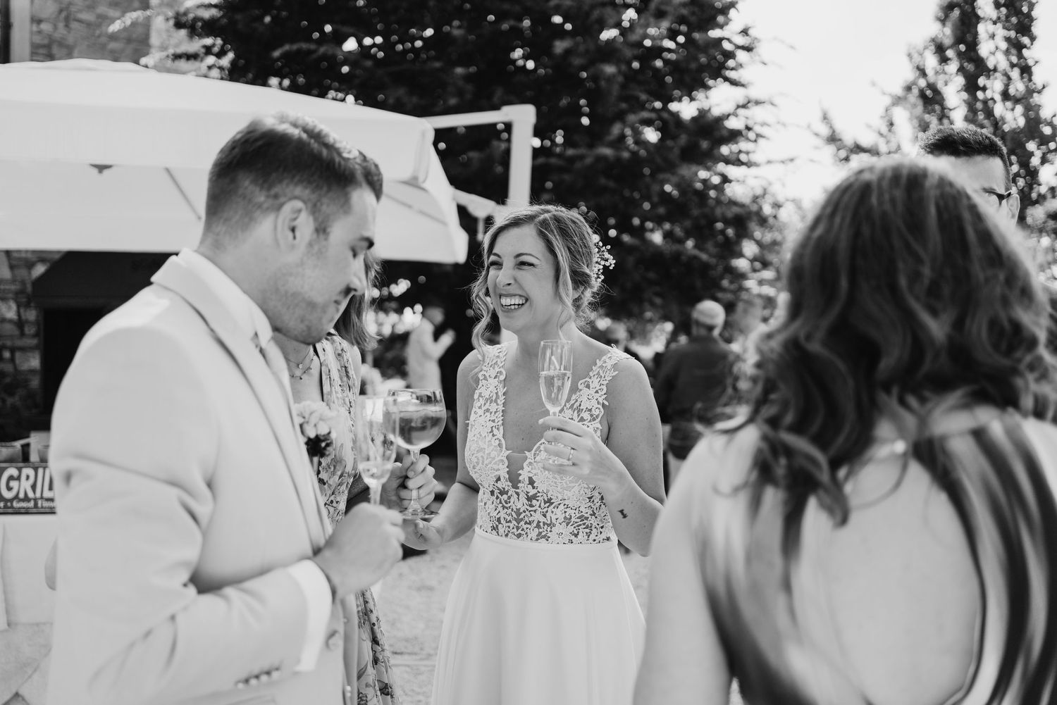 Black and white photo of bride laughing joyfully with groom and guest at outdoor wedding reception.