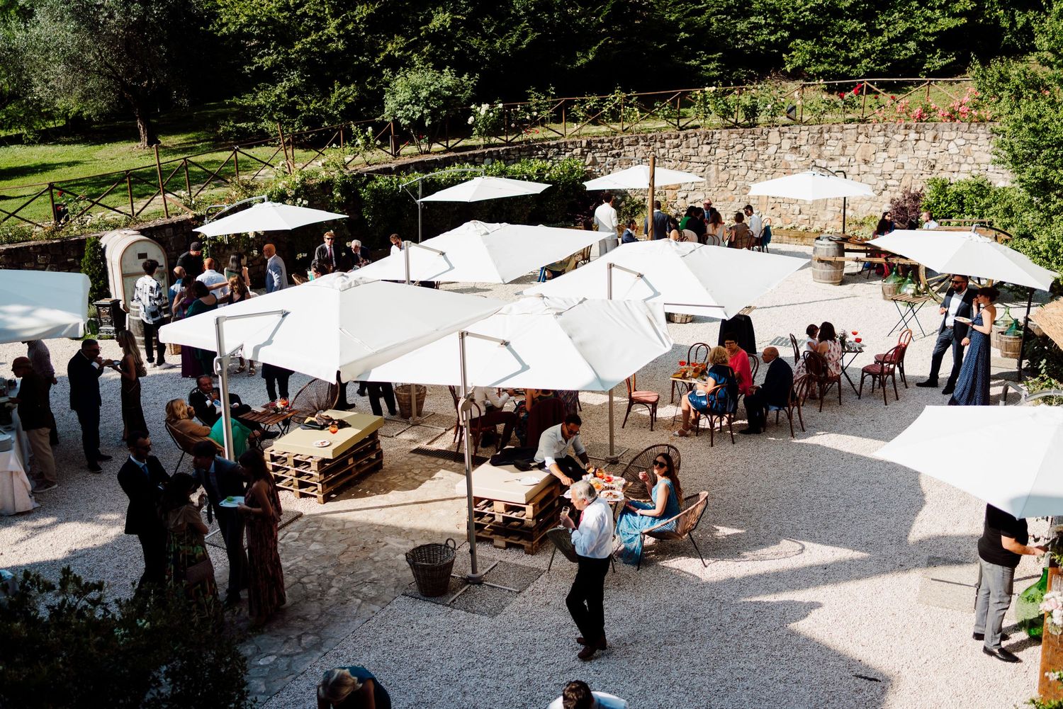 Aerial view of elegant outdoor wedding reception with white umbrellas and wooden furniture.