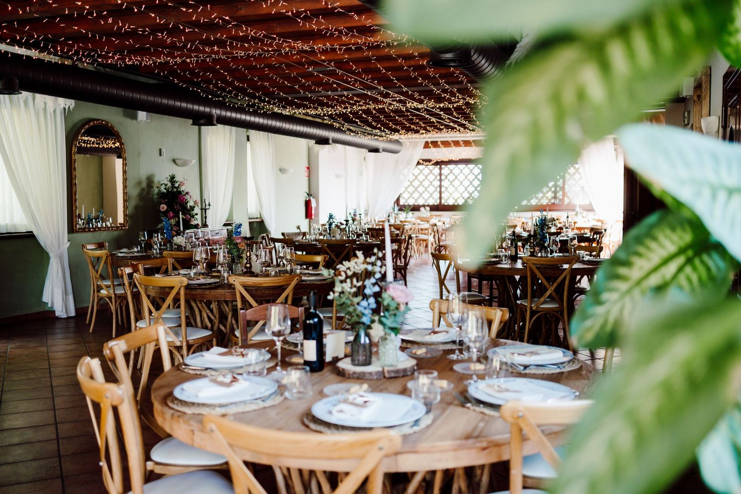 Elegant rustic wedding reception venue with string lights, wooden chairs, and floral centerpieces.