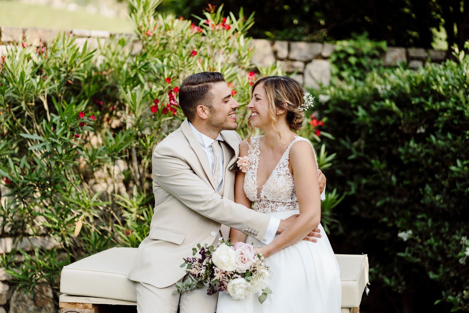 Bride and groom sharing a romantic moment seated outdoors among lush greenery on their wedding day.