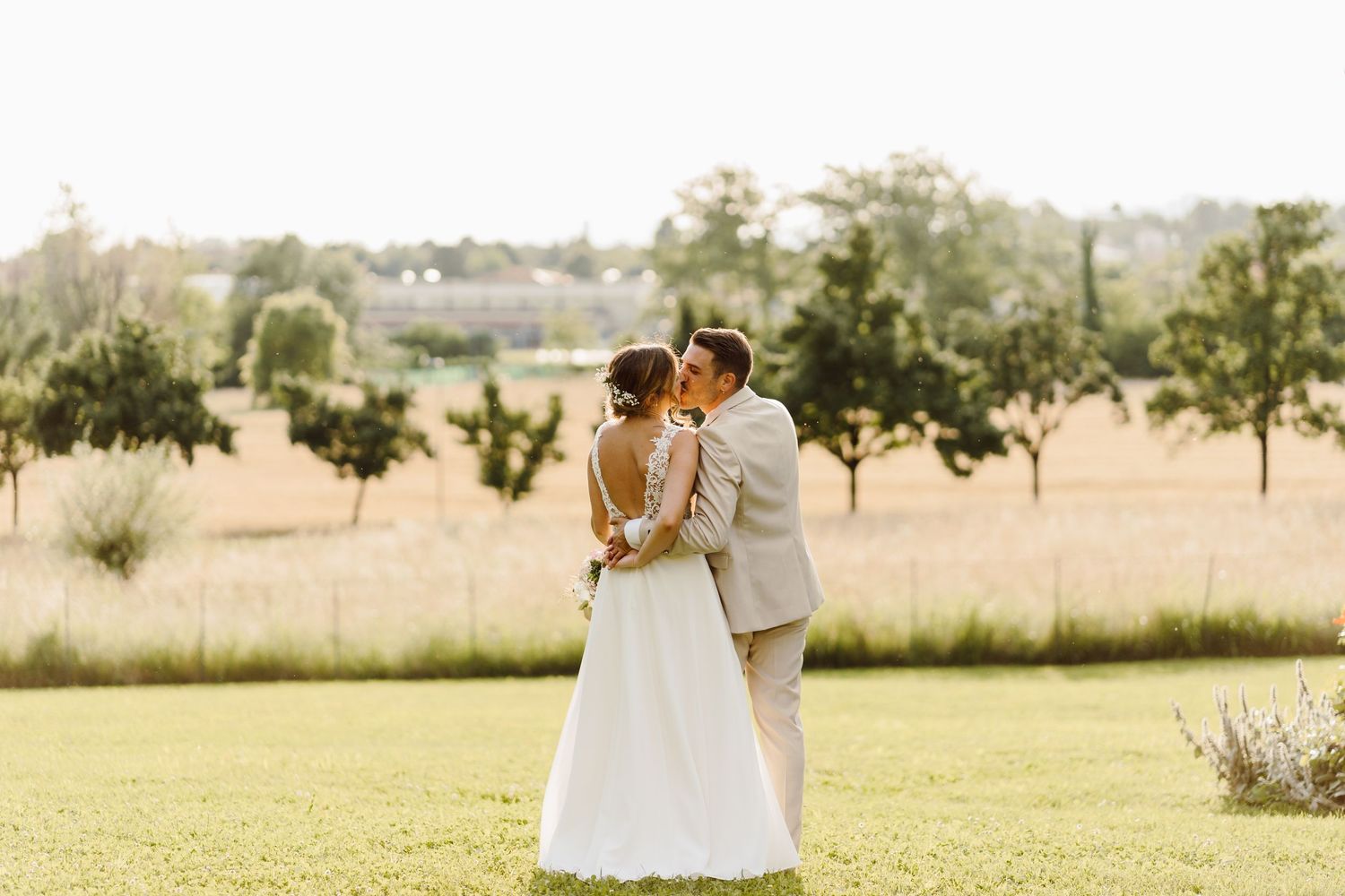 Bride and groom sharing a kiss in a golden sunlit meadow with trees in the background.