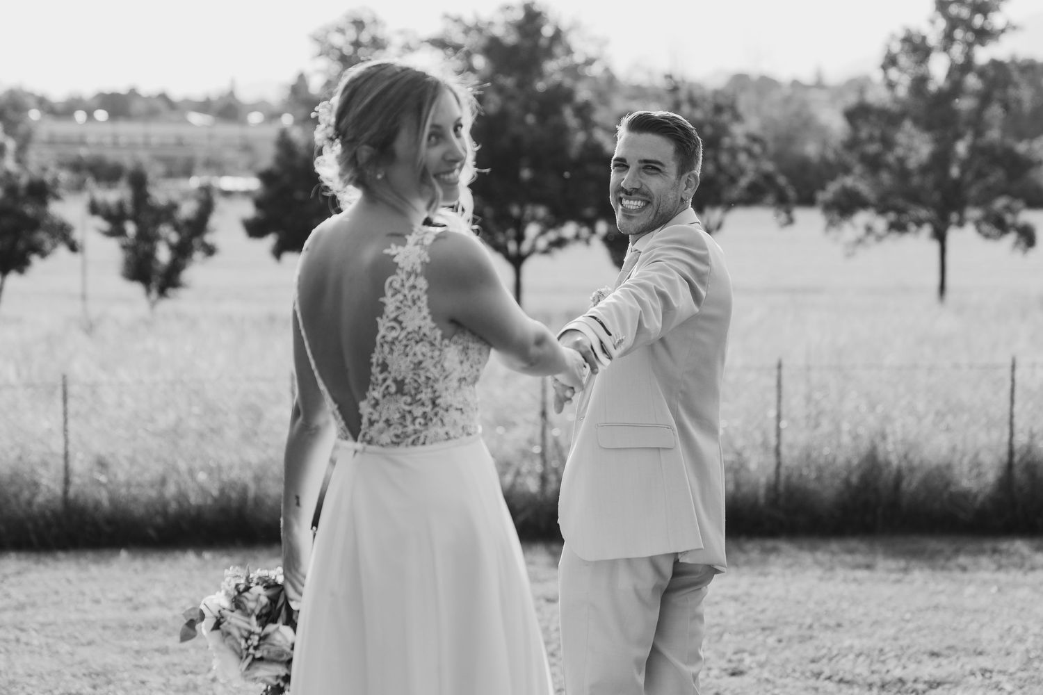 Black and white photo of smiling bride and groom holding hands in an outdoor field setting.