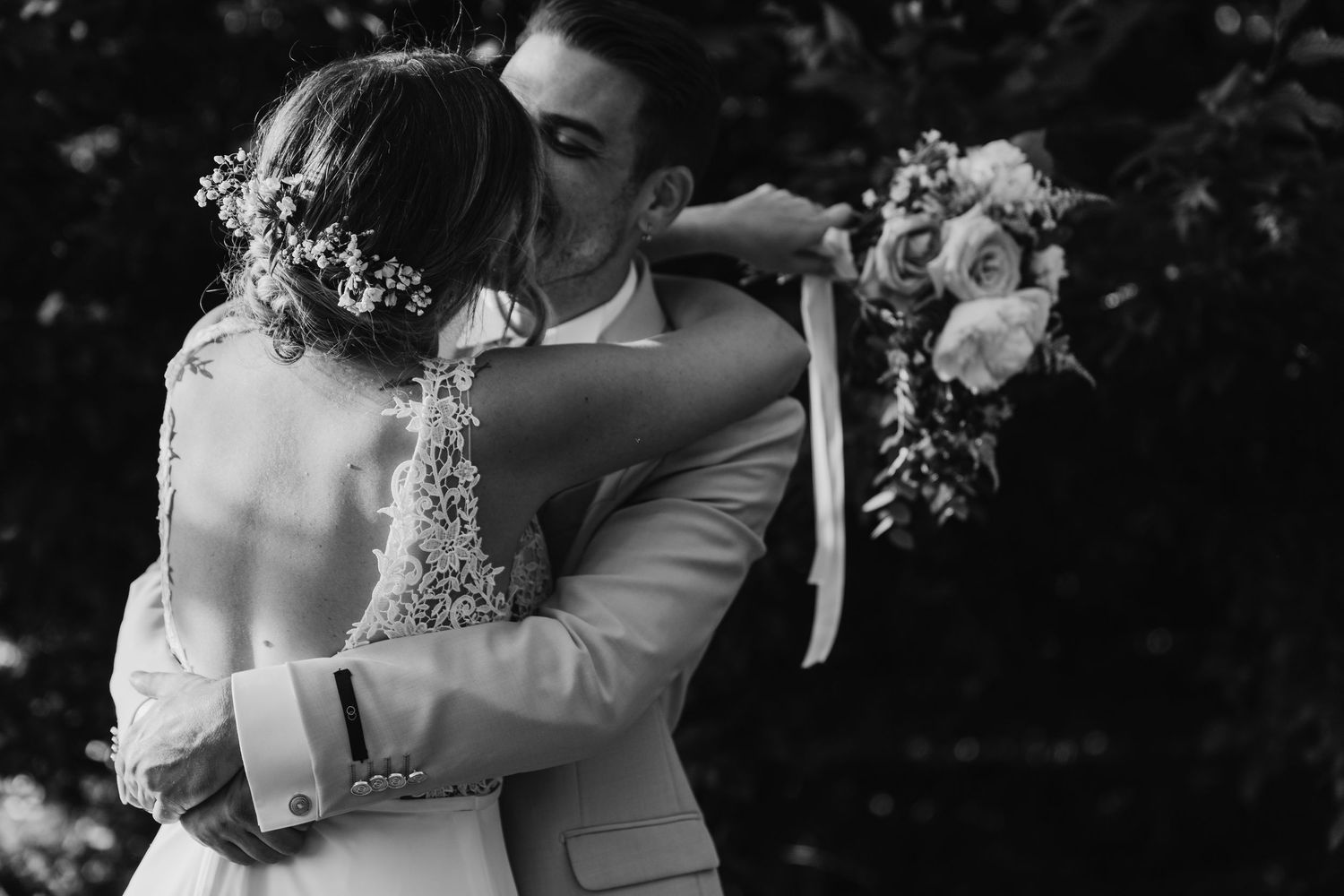 Black and white photo of bride and groom sharing a tender kiss, bride holding a romantic bouquet.
