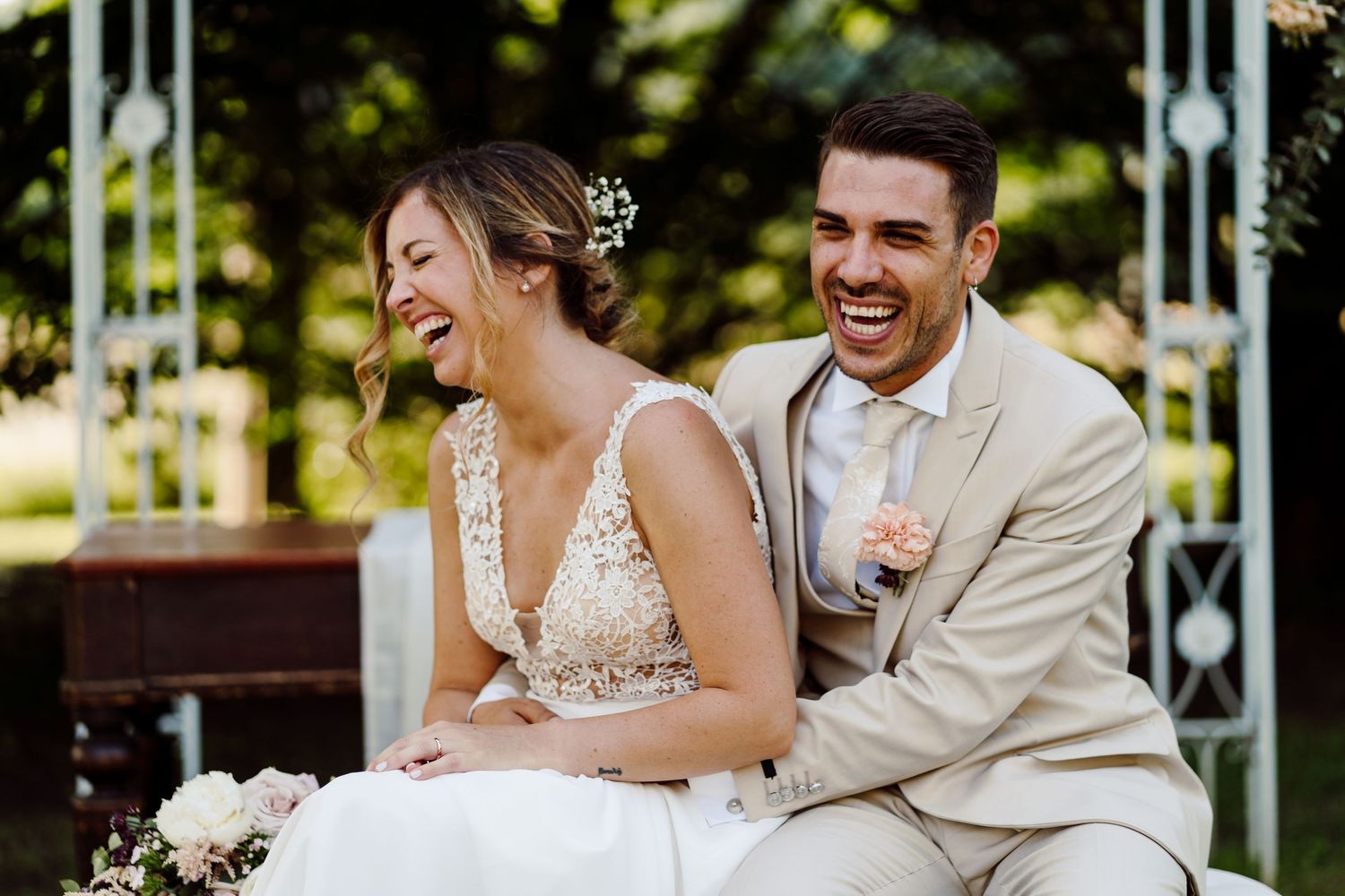 Bride and groom laughing joyfully together while seated outdoors at their wedding ceremony.