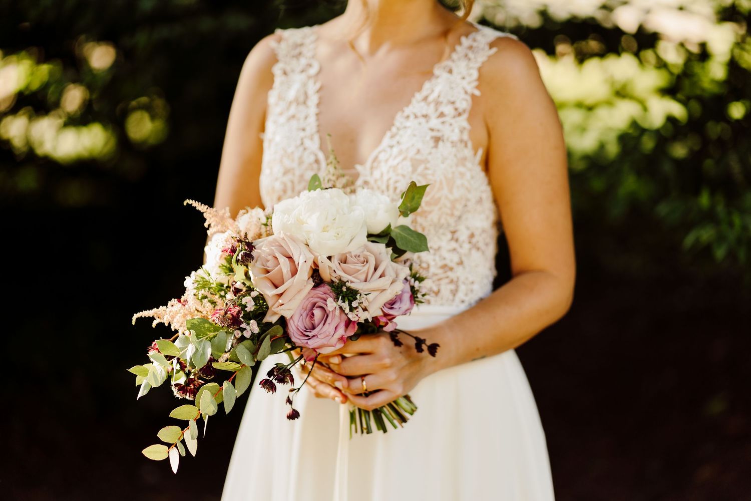 Close-up of bride holding a lush bouquet of pink and white roses in a lace wedding gown.