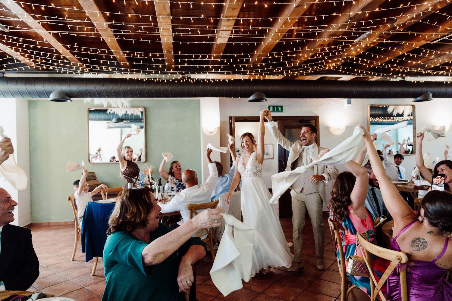 Bride and groom making a grand entrance at their wedding reception as guests cheer and wave napkins.