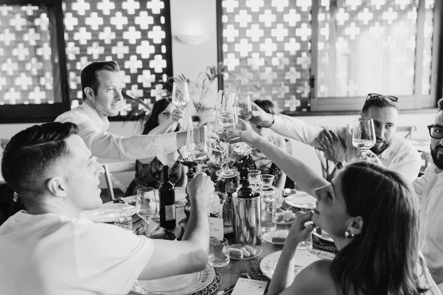Black and white photo of wedding guests raising glasses in a celebratory toast at the reception.