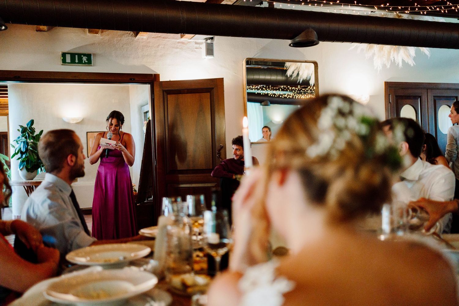 Bridesmaid in purple dress giving a heartfelt speech at an elegant candlelit wedding reception dinner.