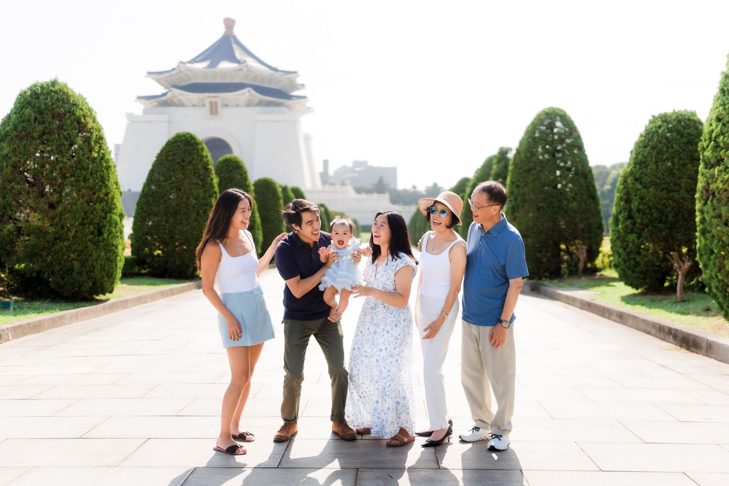 A group of people walking along a scenic pathway with manicured hedges and a castle-like structure in the background.