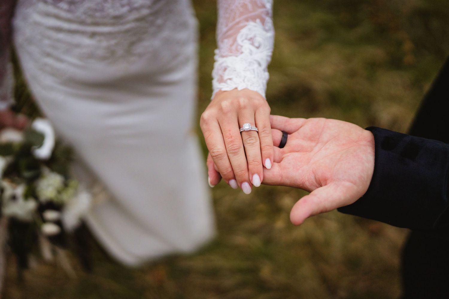 Close-up view of hands exchanging wedding rings during an outdoor ceremony.