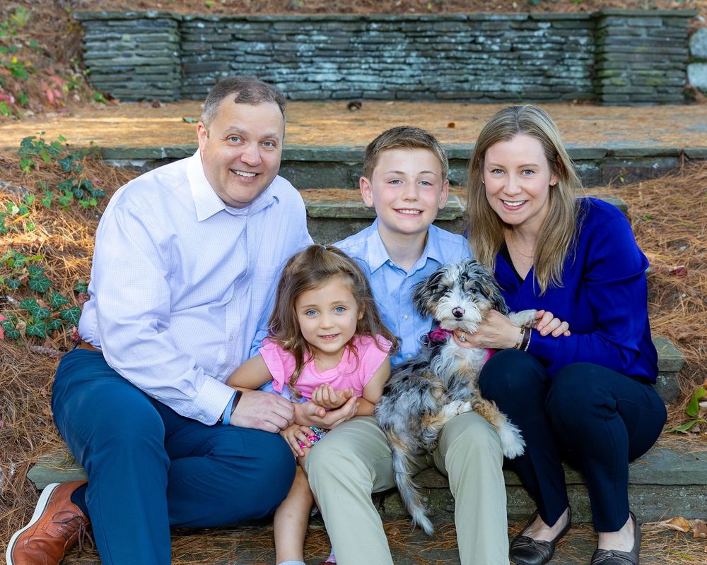 A family sits together on stone steps  with their white and gray puppy during an autumn photo session.