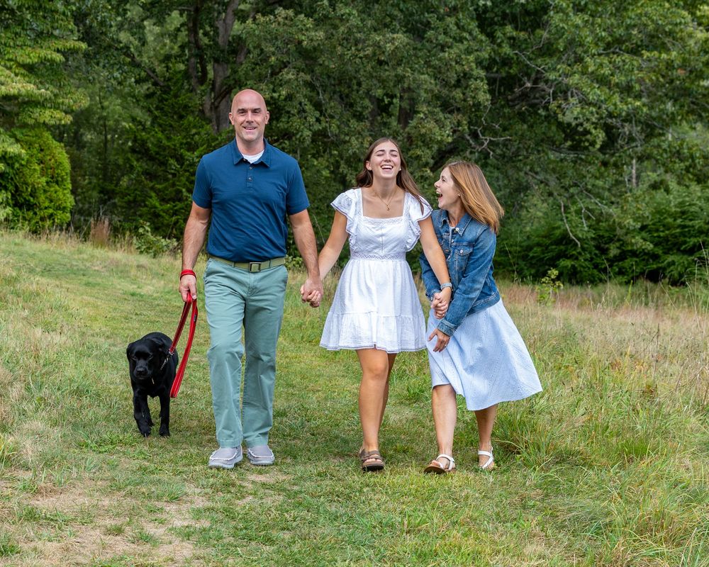 A family walking together laughing through a lush green meadow during high school senior yearbook photo session in Concord, MA.