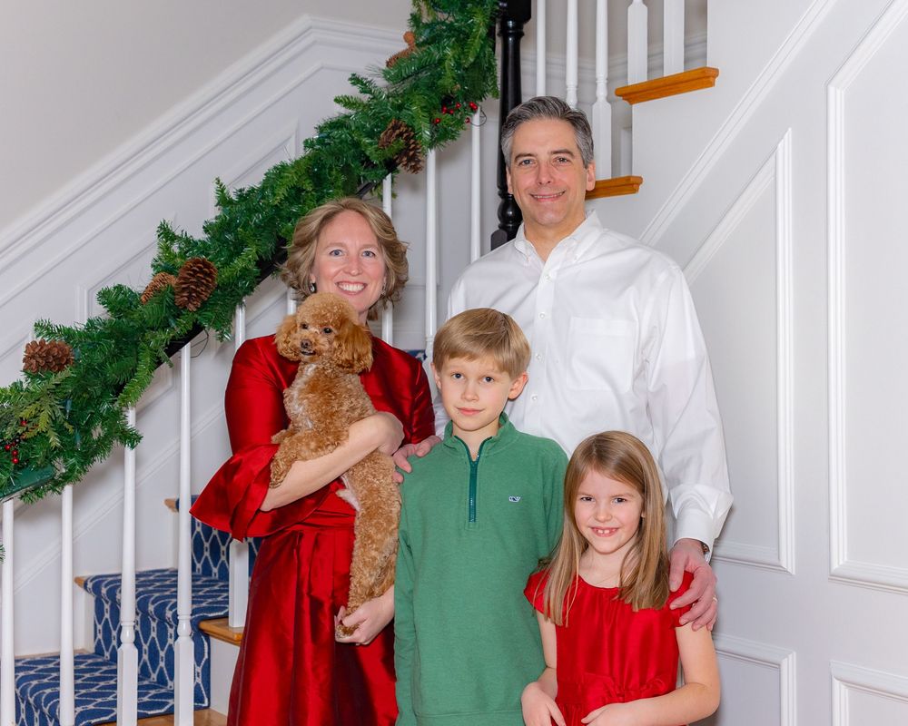 A family poses in front of a decorated staircase during an at home holiday family photo session in Metrowest of MA by Lisa West Photography.
