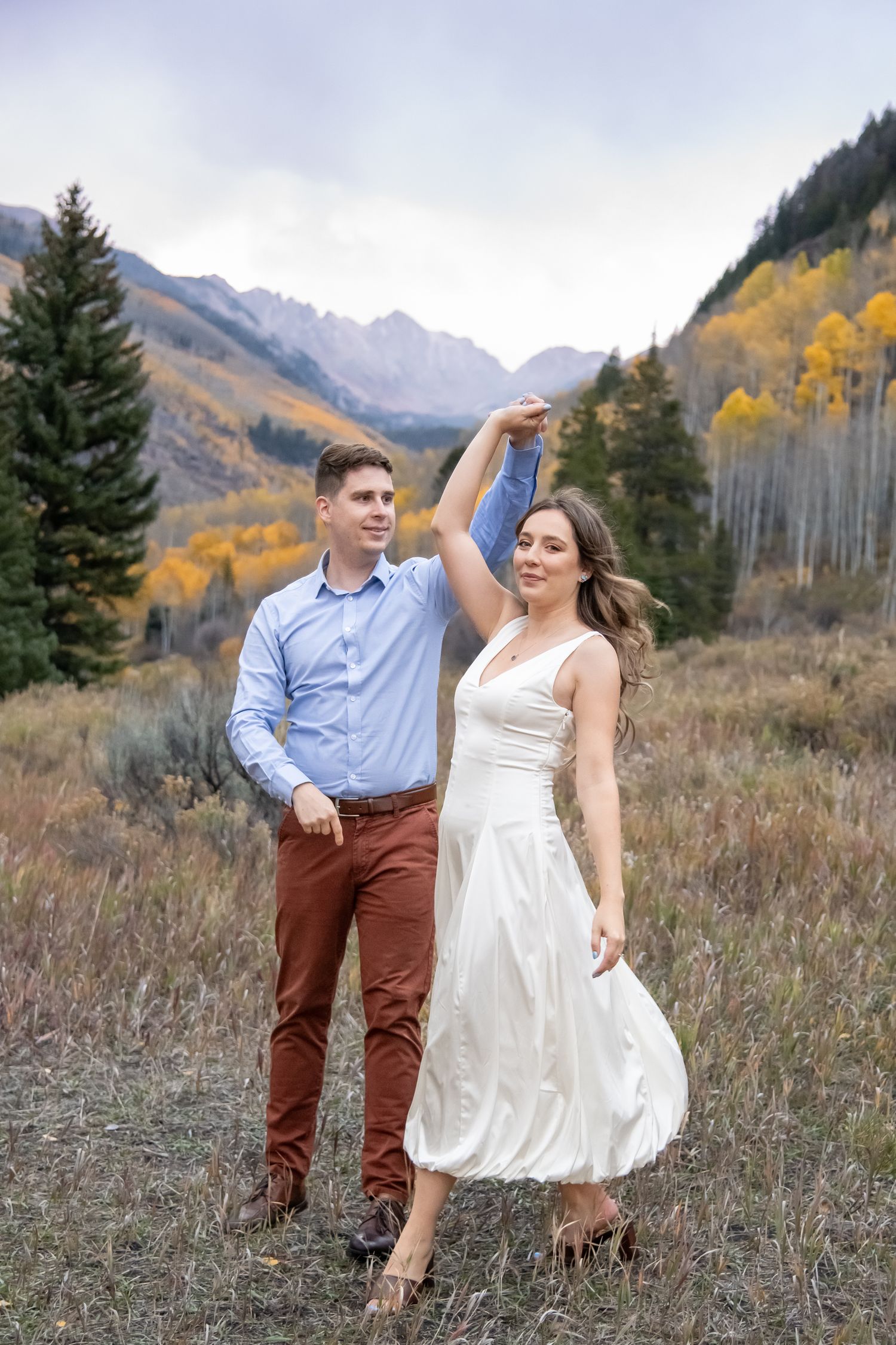 Vail engagement photos Couple dancing together in a mountain meadow with autumn colors and evergreen trees in the background.