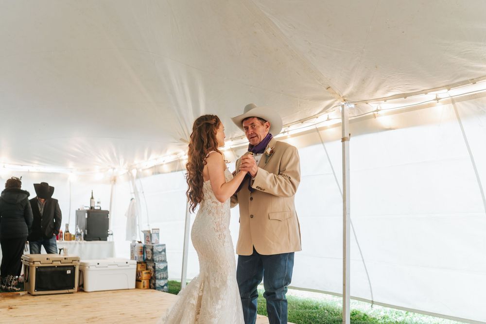 A couple shares their first dance under a white tent at an outdoor wedding reception.