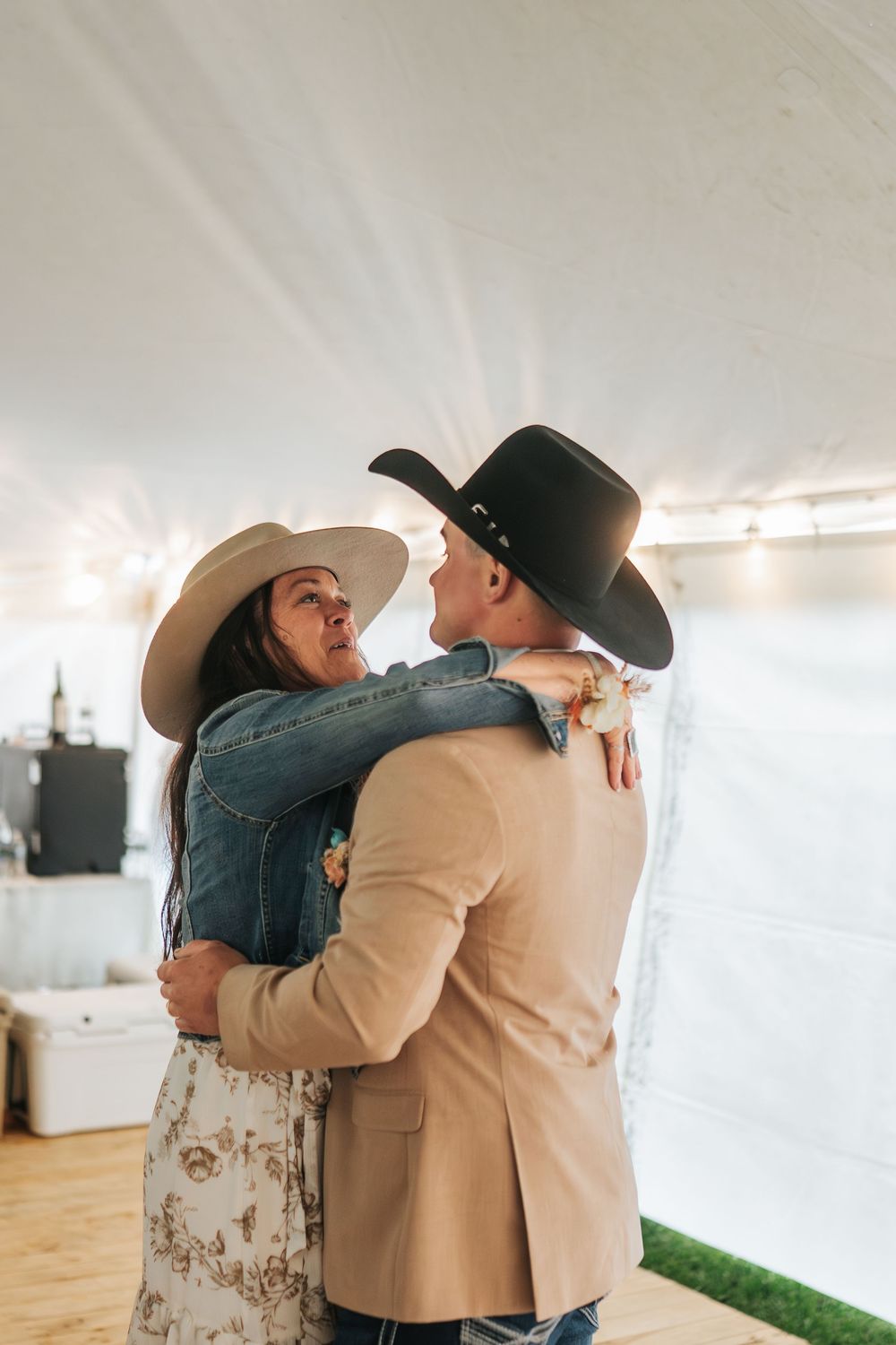A couple in western attire share an intimate dance moment under a white tent at an outdoor event.