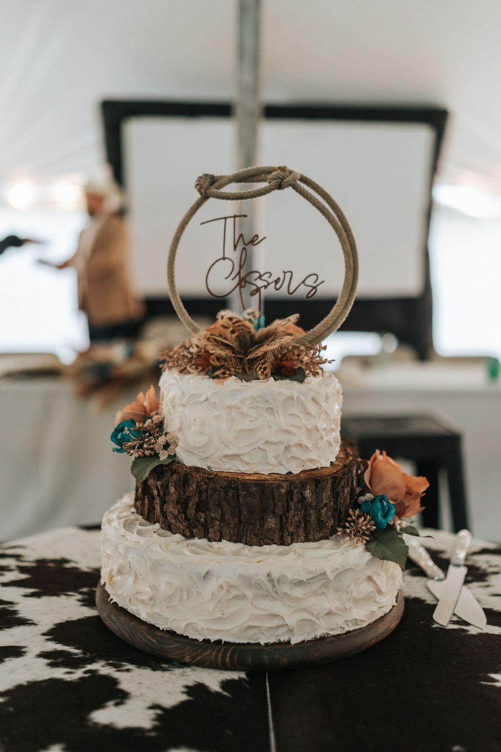 A rustic white wedding cake with multiple tiers decorated with flowers and a wooden base cake topper.