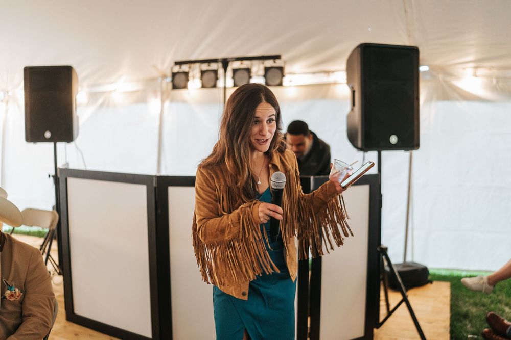 A person in a brown fringe jacket stands in front of a white tent during an outdoor event.