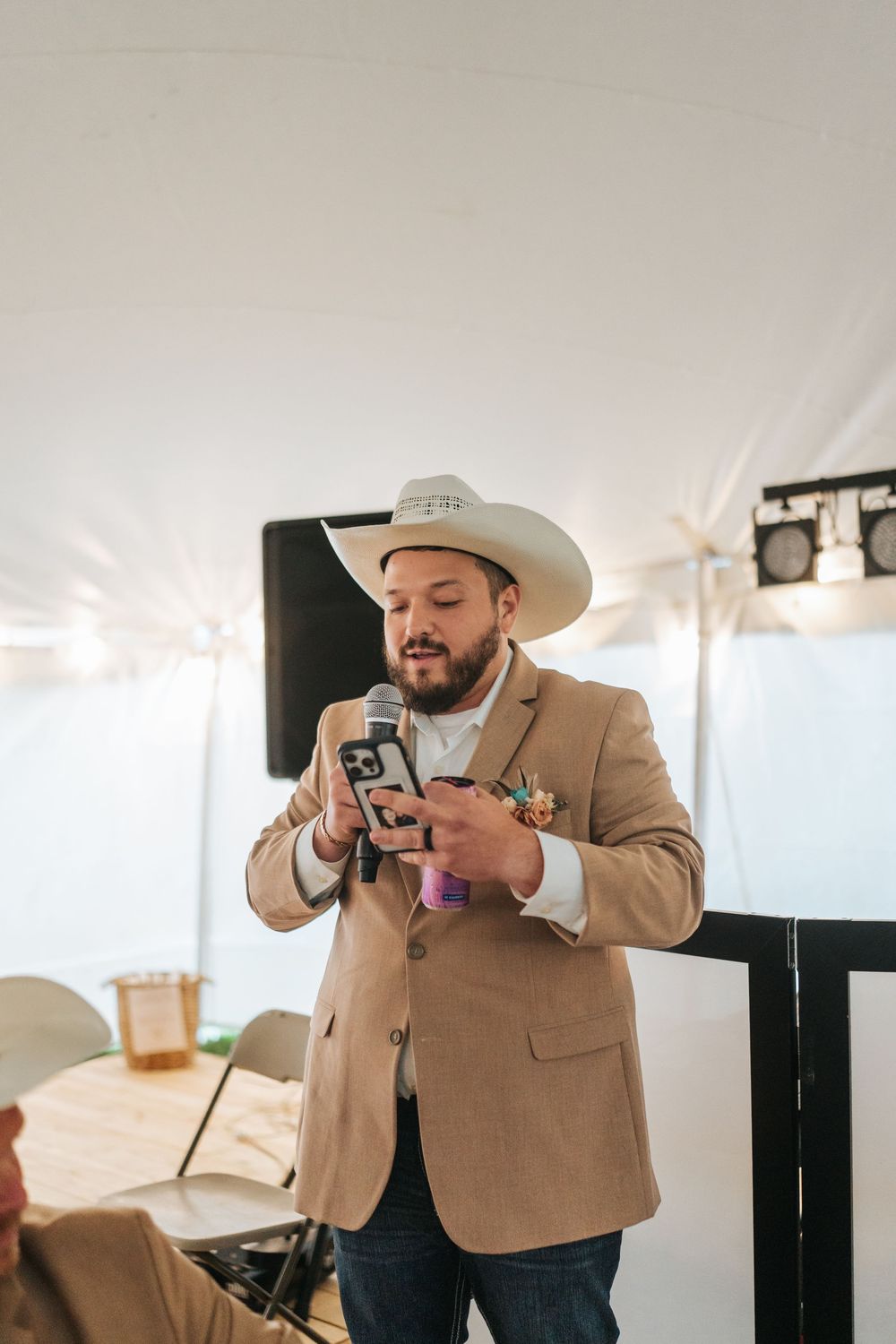 A person in a tan blazer and cowboy hat takes photos with a camera at an indoor event.