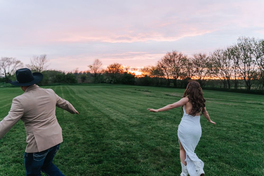 Silhouettes of two people dancing and twirling in a green field at sunset with dramatic orange sky.