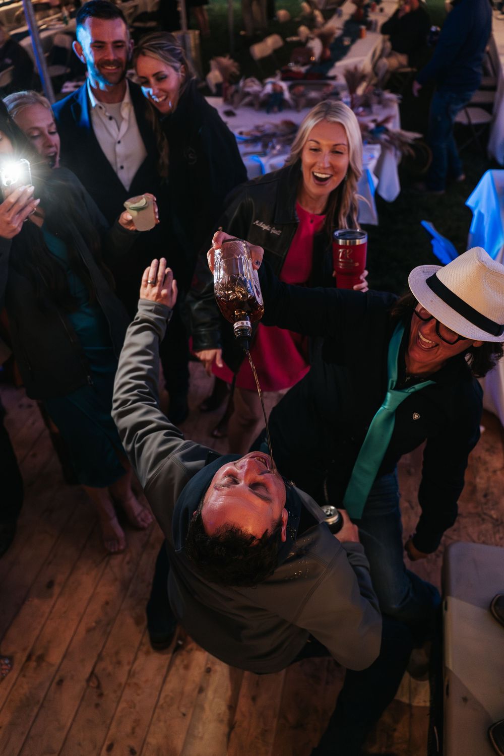 People dancing and celebrating on a wooden dance floor at a dimly lit party venue.