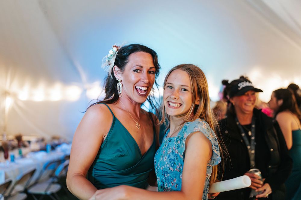 A group of guests celebrate and dance together under a white tent at a festive evening party.