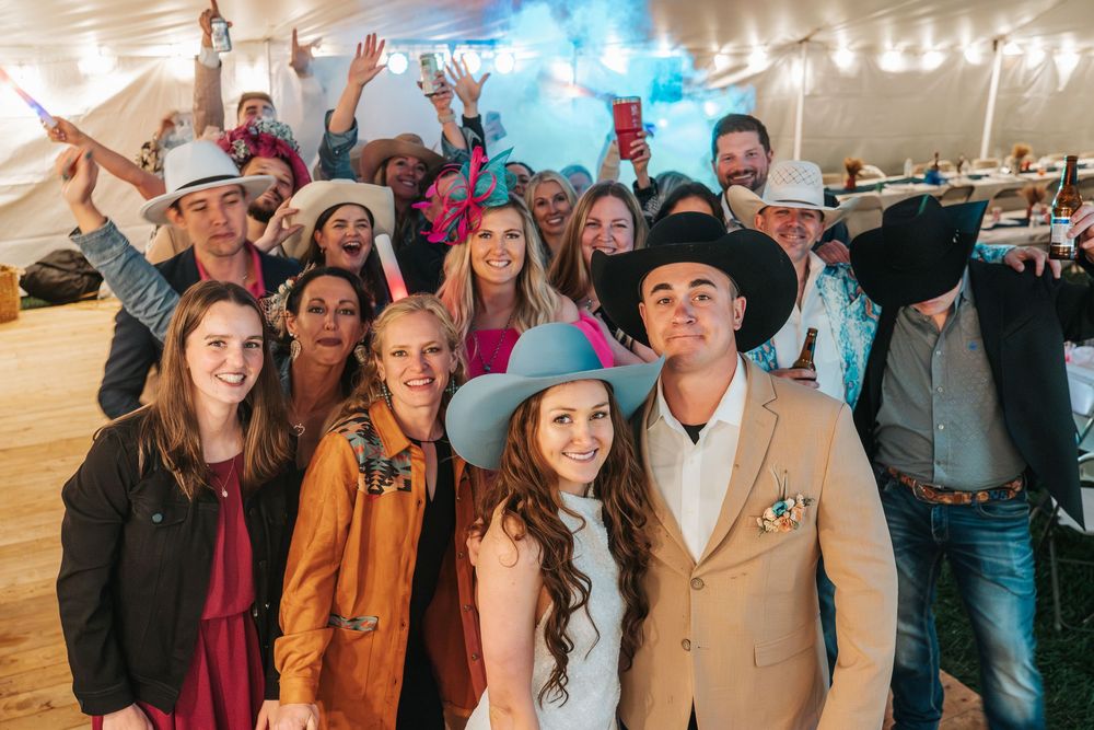 Wedding guests celebrate and pose together under string lights at an outdoor reception venue.