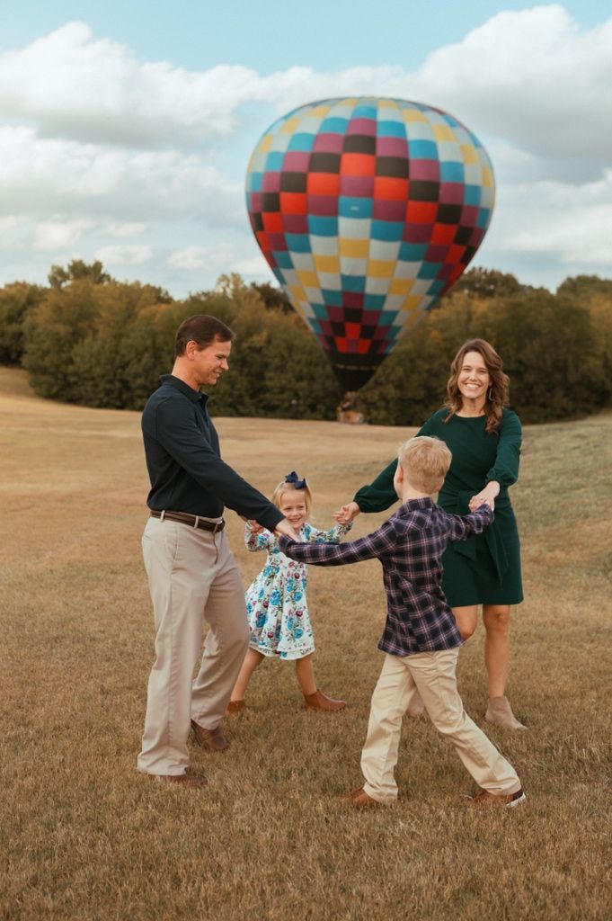 A colorful hot air balloon provides backdrop for playful family photos in a grassy field.