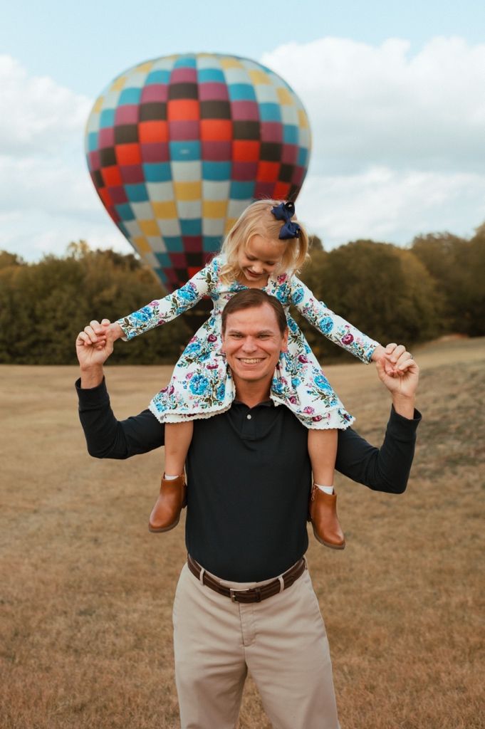 Playful moment captured in front of a colorful hot air balloon in an open field.