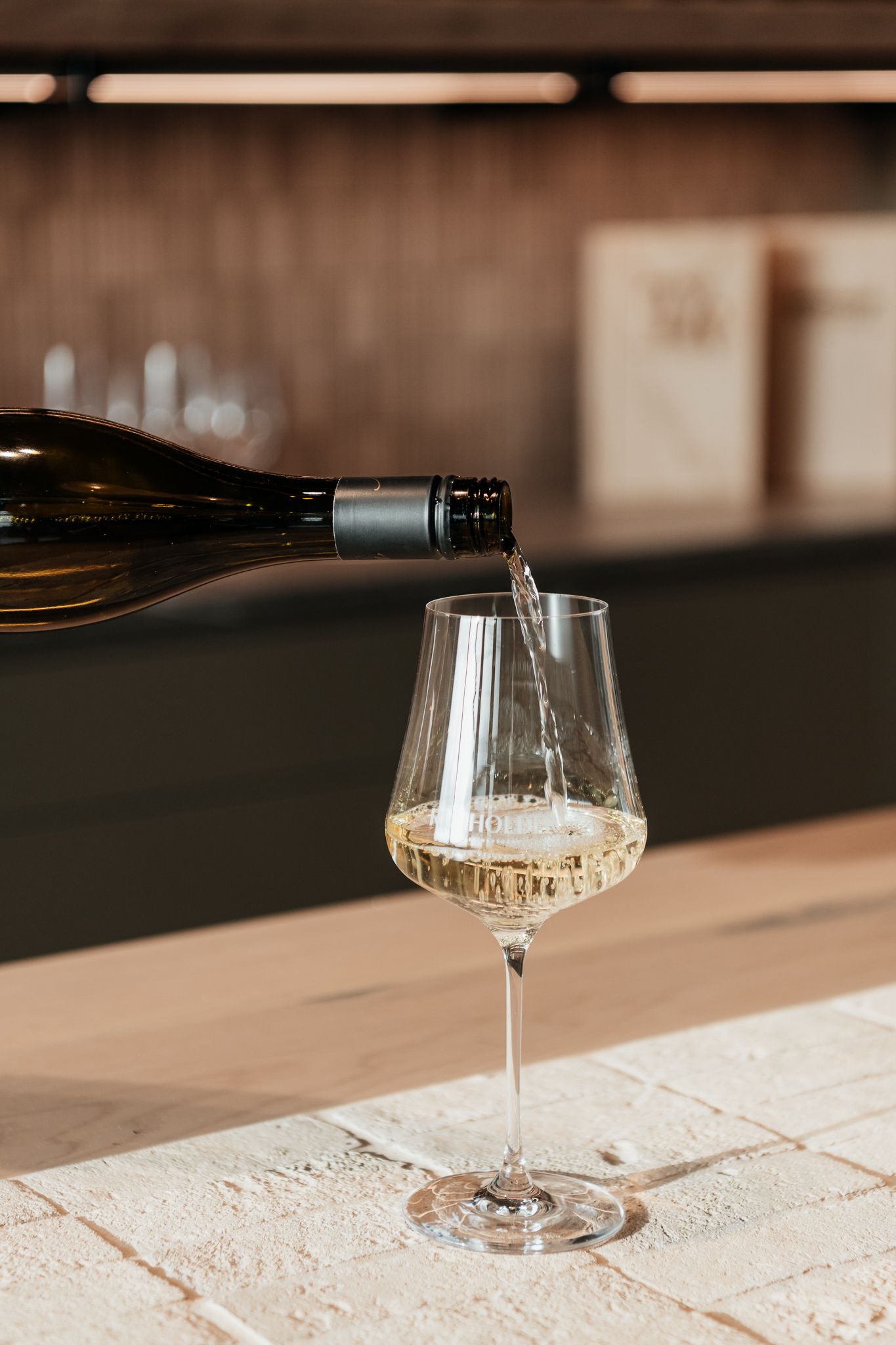 Wine being poured into an elegant wine glass on a white textured surface in warm lighting at The Runholder by August and Vine