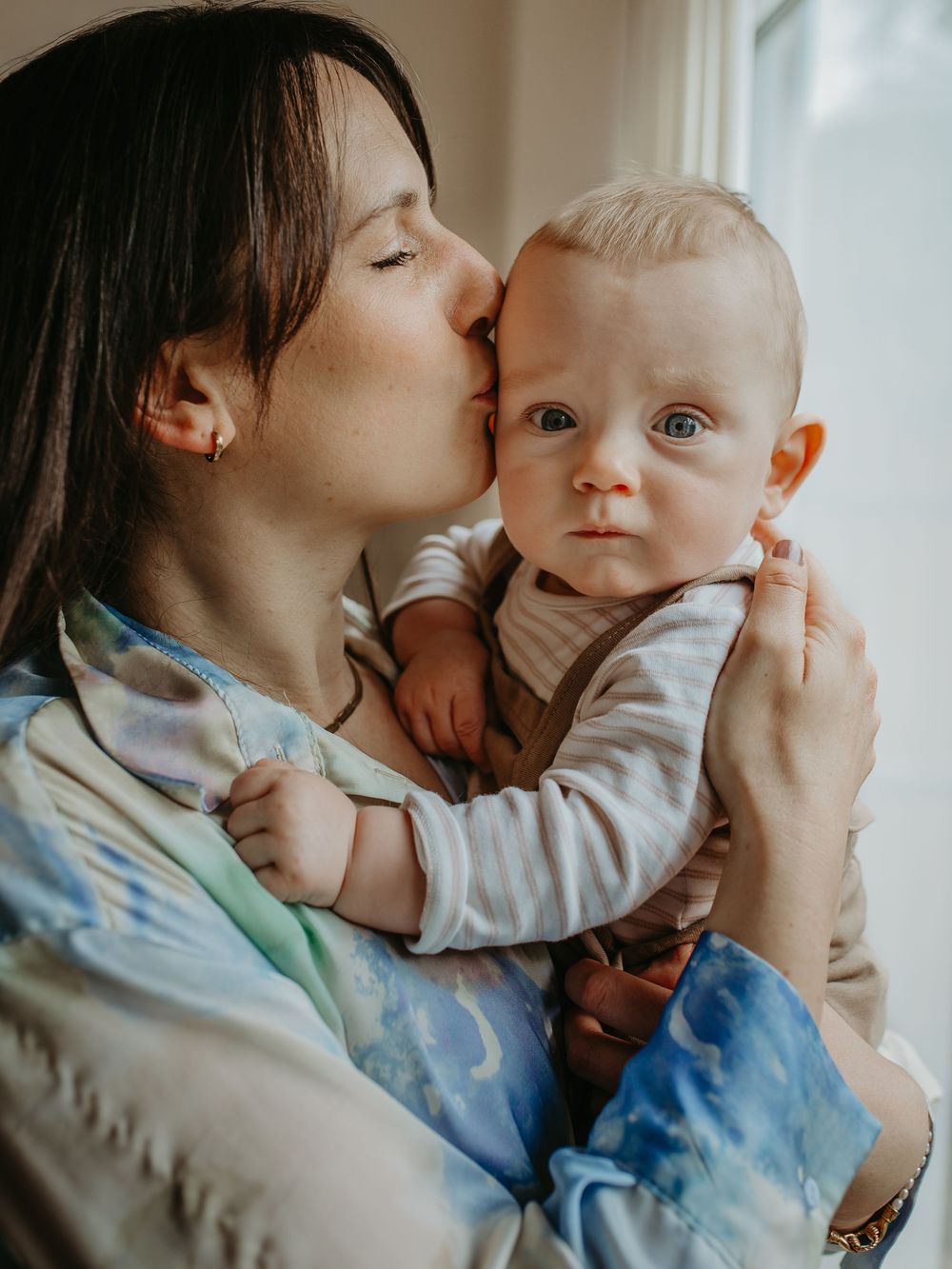 A tender moment captured in a series of intimate photos showing gentle kisses and cuddles with a baby in soft lighting.