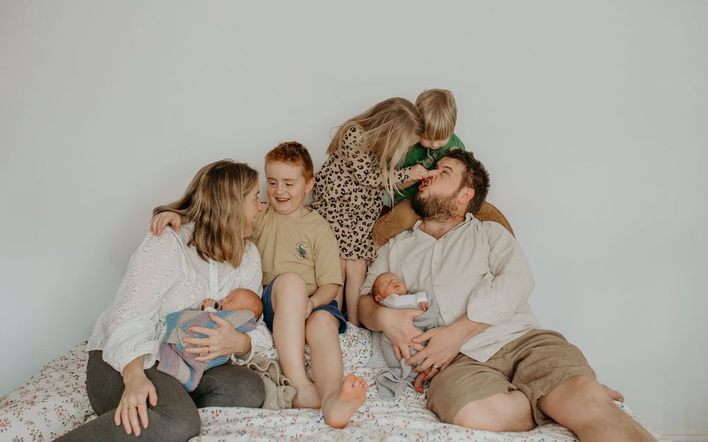 A series of candid lifestyle photos showing tender moments between family members relaxing together on a white bed.