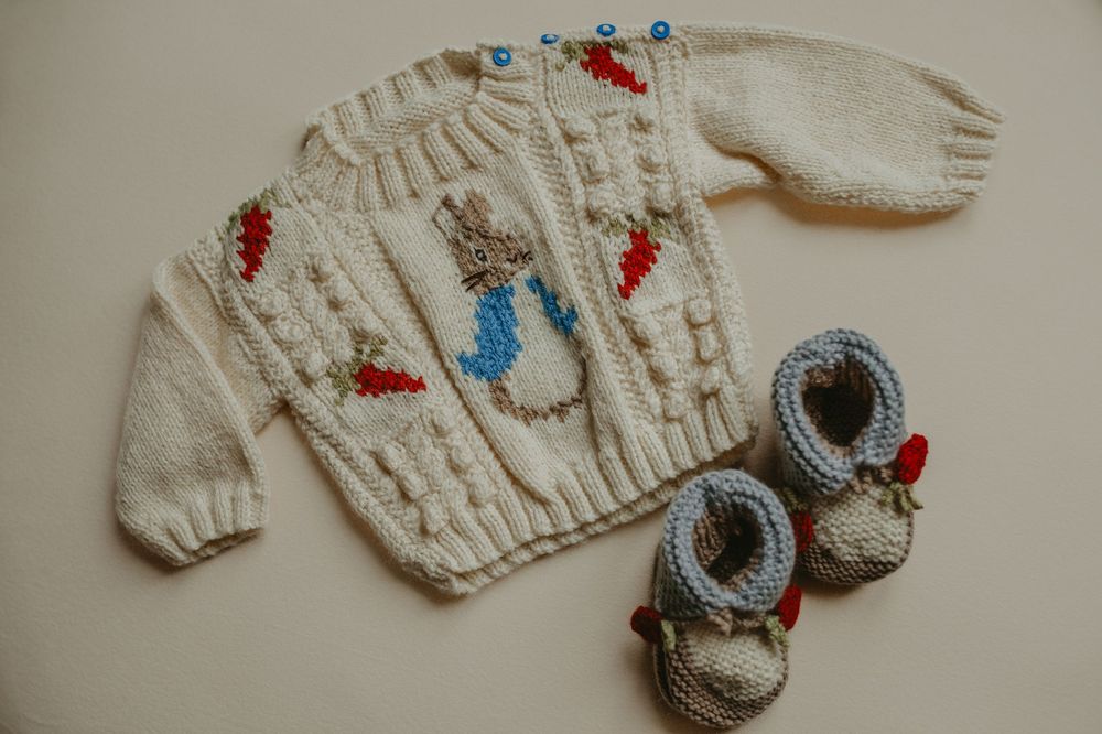 Handmade cream-colored baby sweaters and booties with delicate red floral embroidery details displayed in a row.