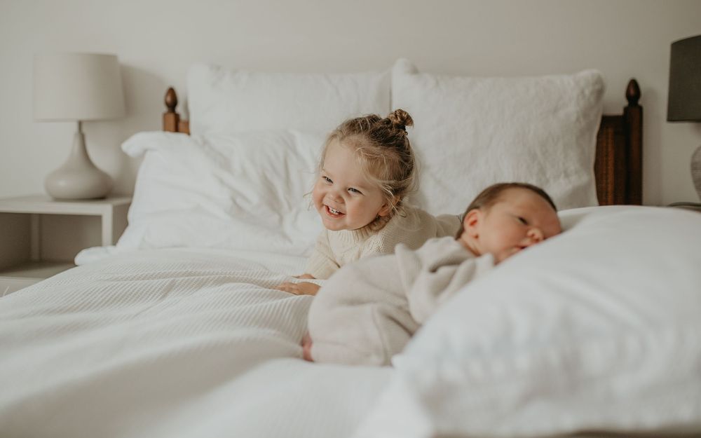 Tender moment captured in soft white bedding showing gentle interaction with a sleeping infant.