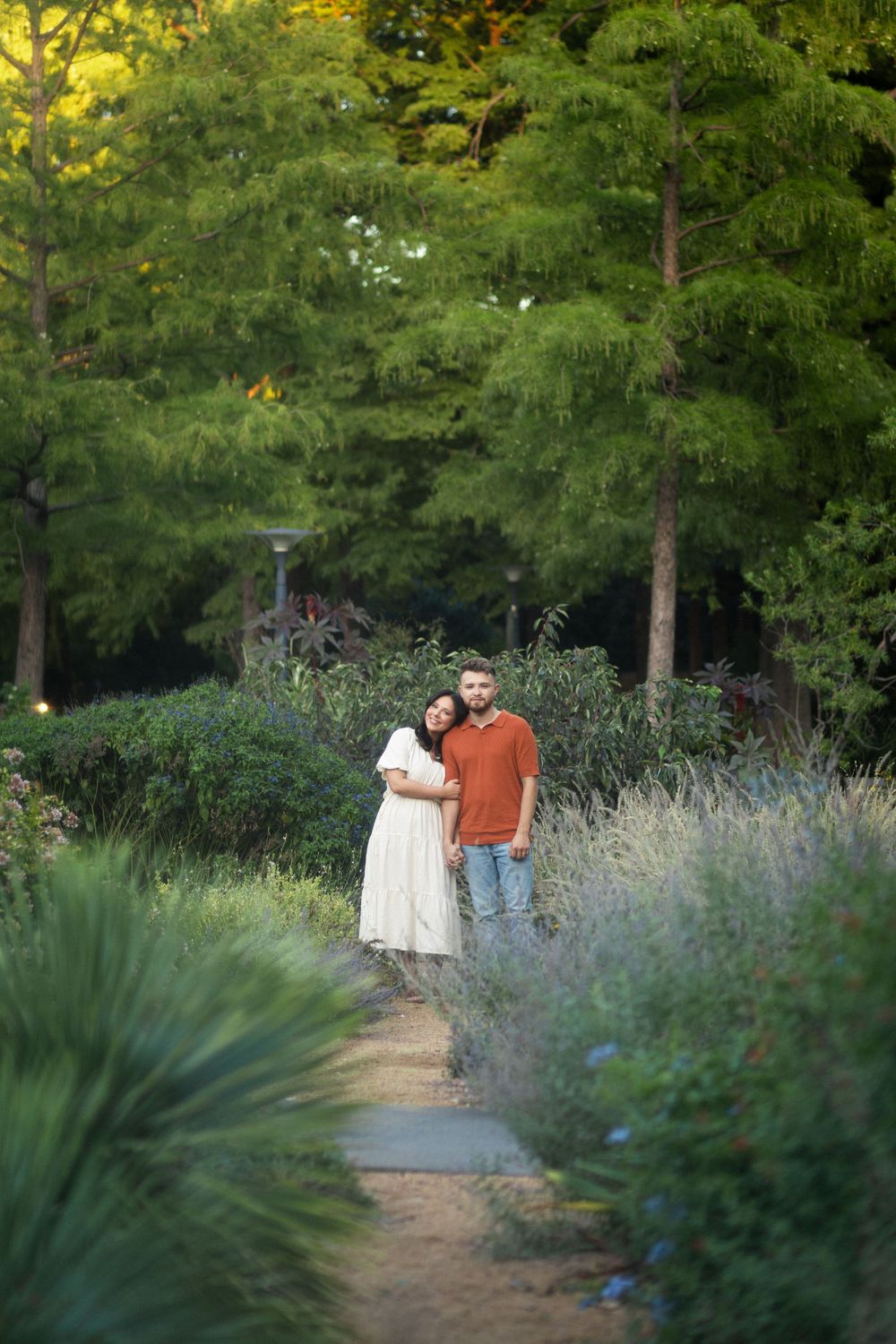 Couple embracing on garden path surrounded by lush greenery.
