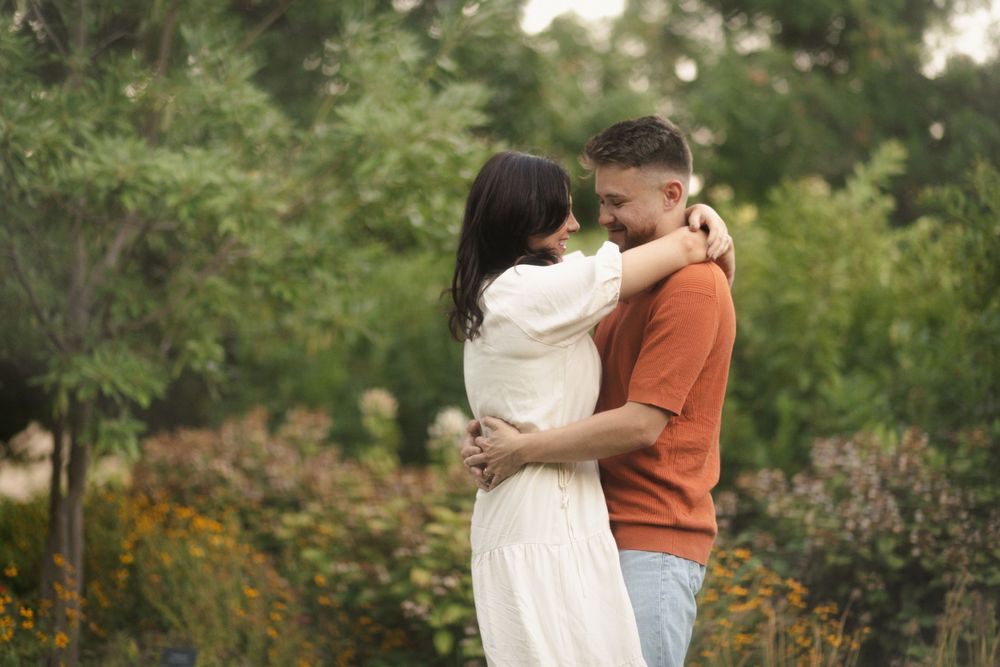 Romantic couple embracing in garden setting with person in orange sweater and white dress.