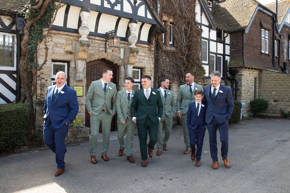 Groomsmen in coordinated suits walking together on cobblestone path near historic buildings.