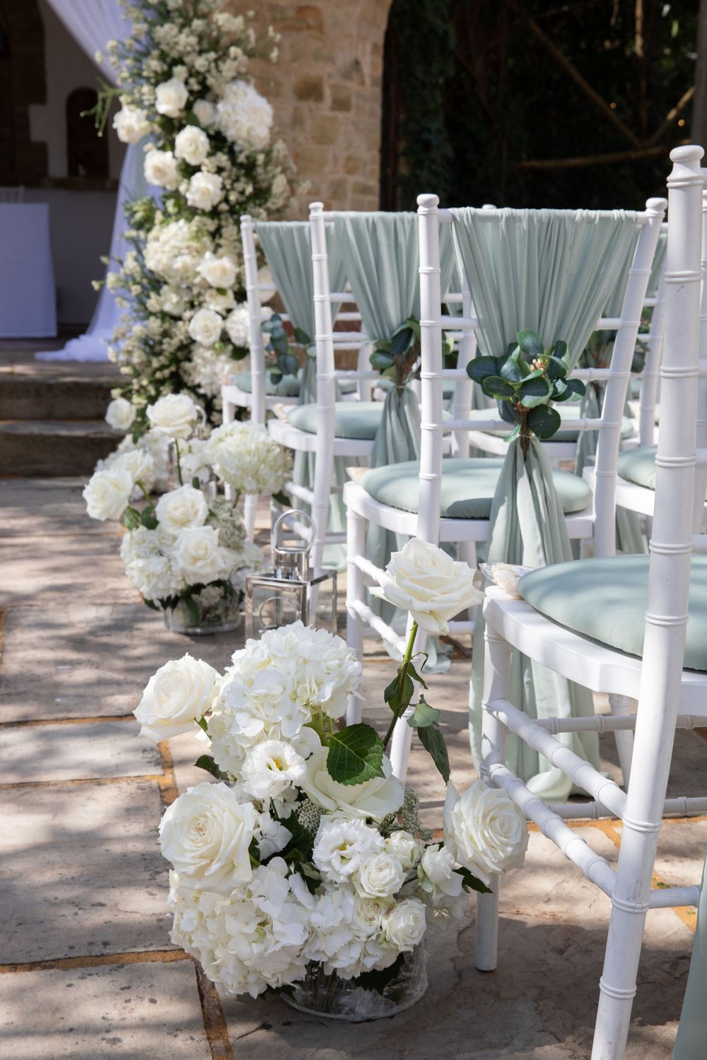 Outdoor wedding ceremony setup with white chairs decorated with mint green sashes and white floral arrangements.