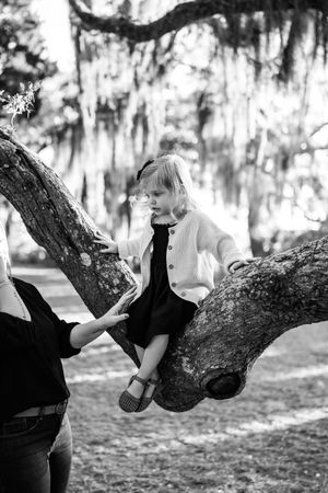 Black and white photos of someone resting on a curved tree branch in a park.
