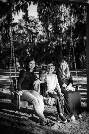 Family enjoying time together on swings in a park with Spanish moss trees.