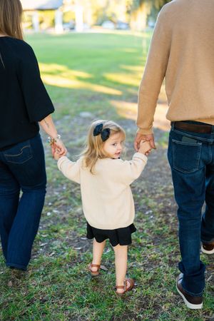 People holding hands while walking together on grass under oak trees.