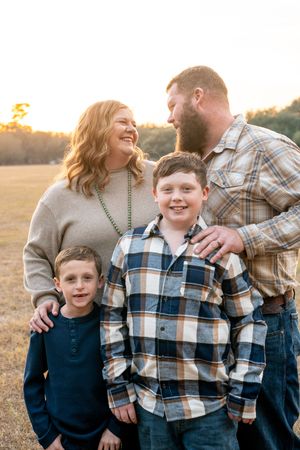 Family shares candid moments of laughter and joy during outdoor photo session at golden hour in a field.
