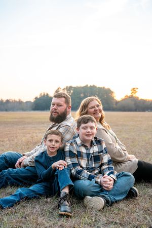 Family lying together in a grassy field during golden hour wearing casual plaid clothing.