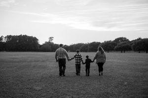 A family walks together holding hands in a black and white photo across an open field at dusk.