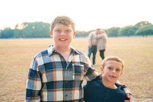 Family in plaid shirts smiles and laughs together while walking through a sunny autumn field.