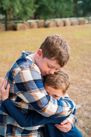 Two people in plaid shirts embrace in a heartfelt moment outdoors on an autumn day.