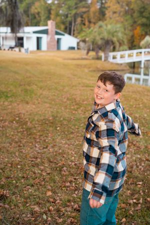 Someone wearing a plaid flannel shirt and teal pants stands on autumn grass with a white fence in the background.