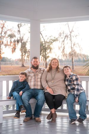 A family of four sits together on a white gazebo bench during sunset with Spanish moss trees in the background.