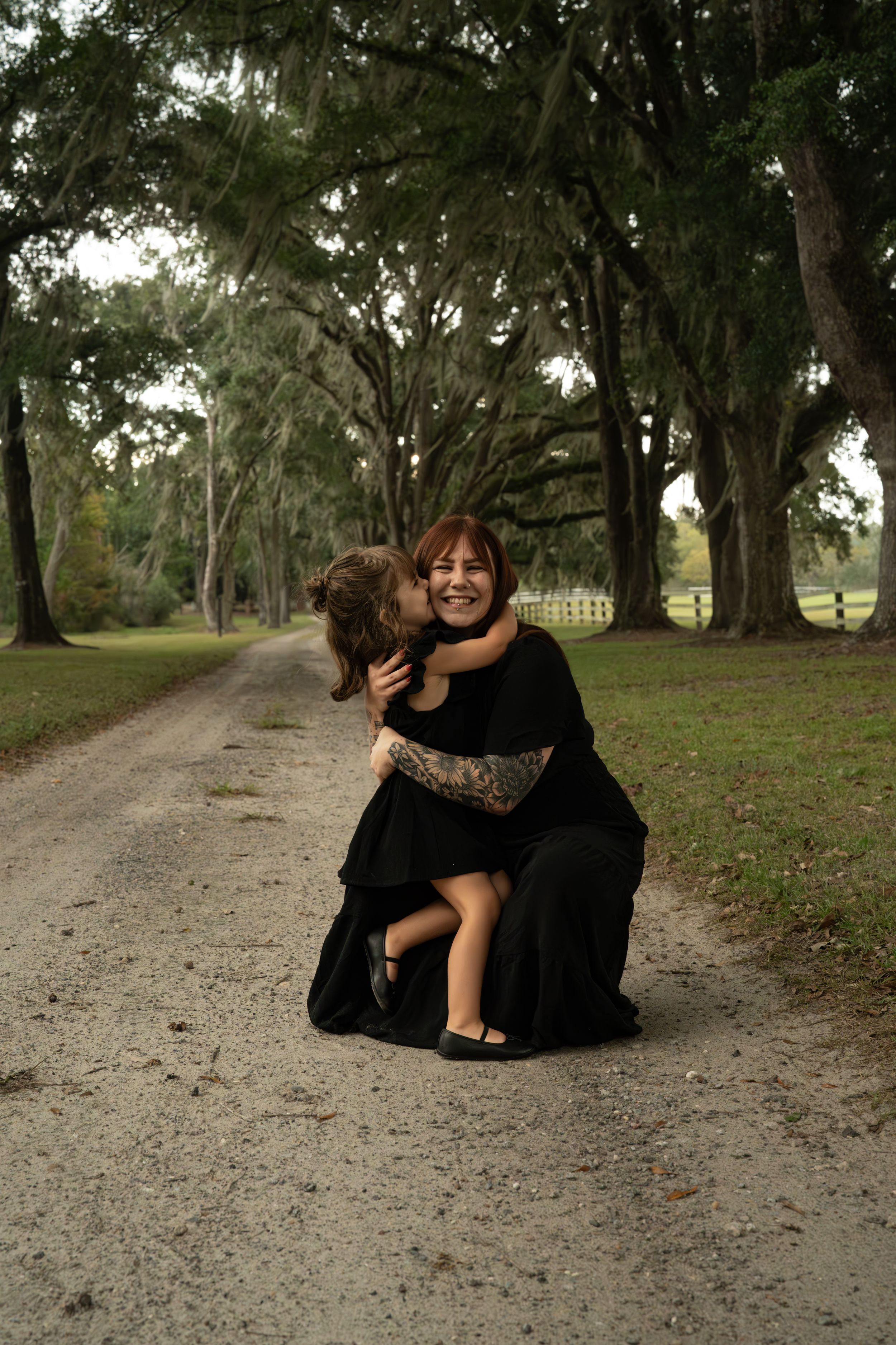 Two people sharing playful moments on a tree-lined gravel path.